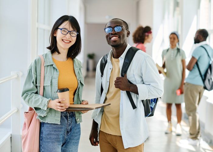 Portrait of multiethnic couple of students smiling at camera standing together at school corridor