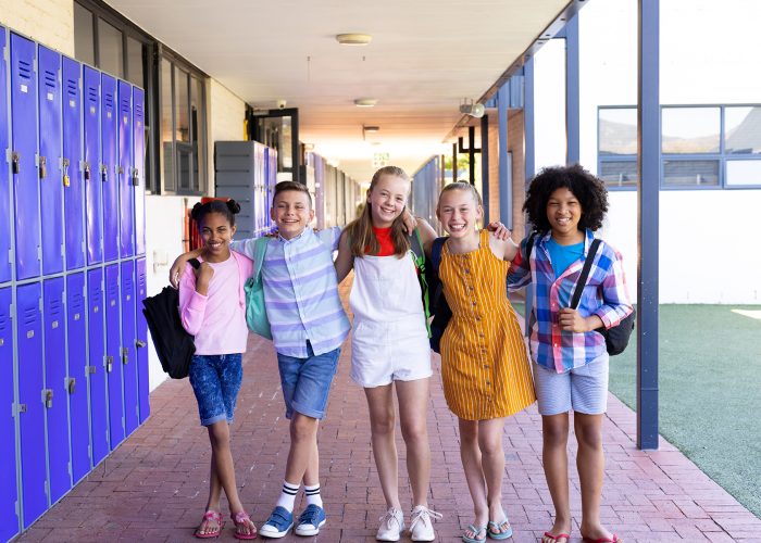 Portrait of five happy, diverse children with arms around shoulders in school corridor. Education, inclusivity, elementary school and learning concept.