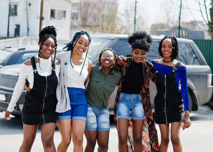 Group of five african american woman walking on road together against suv car on parking.
